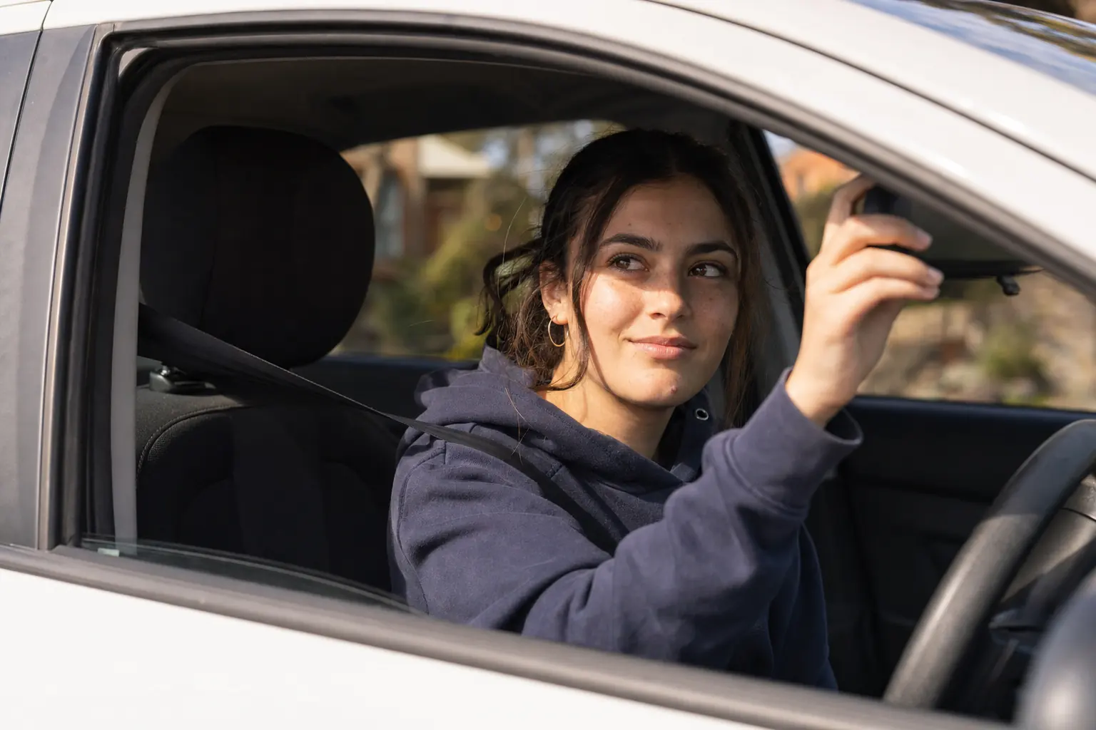 A learner driver adjusting the rear-view mirror before her lesson