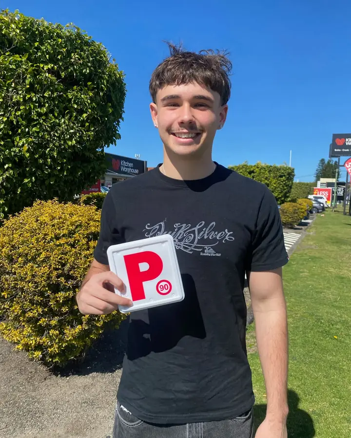 A student holding up his P plate after passing his test