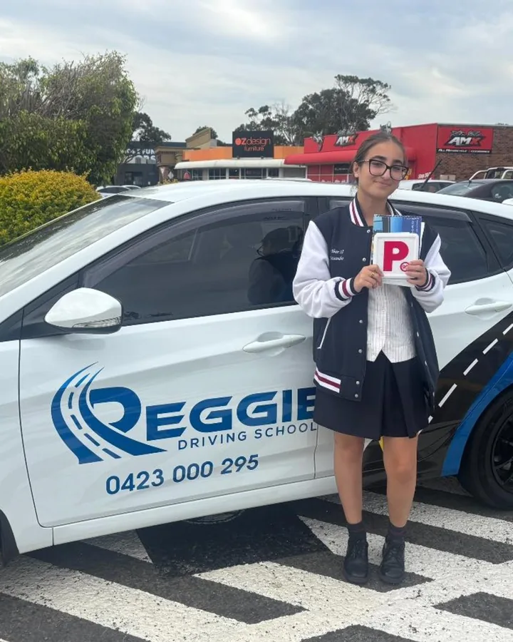 A student in her school uniform holding her P plate beside Reggie's car