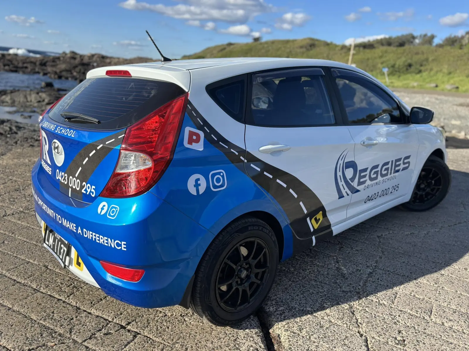 Reggie's Driving School car, a white and blue Hyundai hatch, parked by the water at Shellharbour