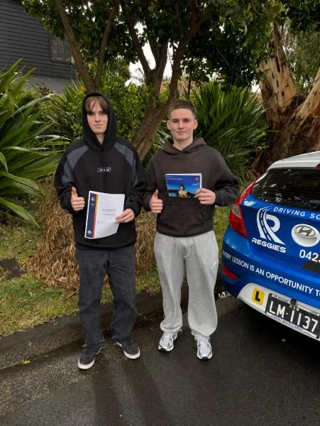 Two students holding their Safer Drivers Course certificates beside Reggie's car